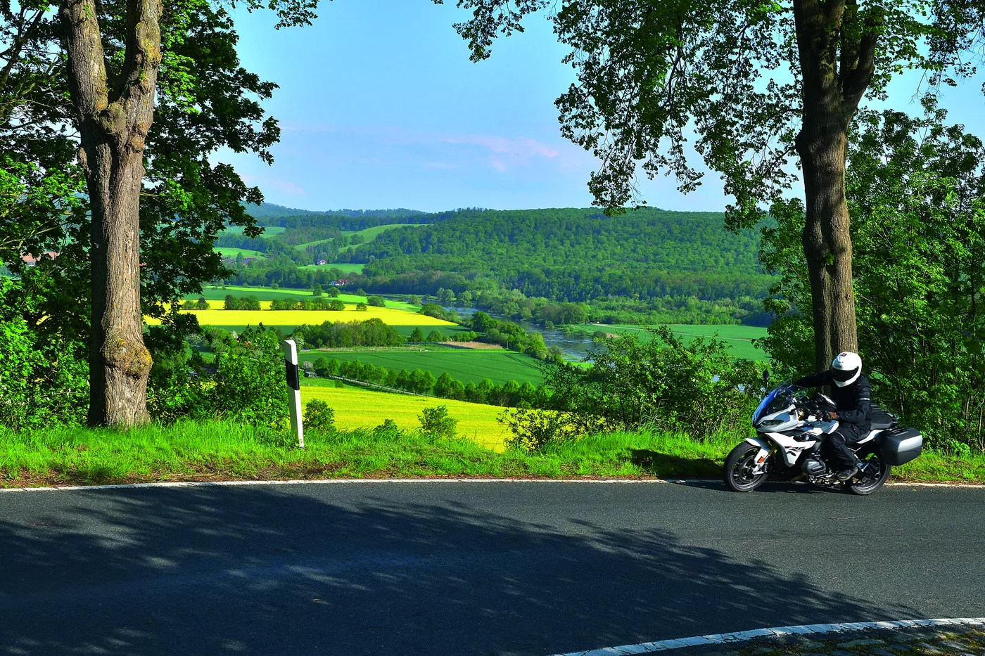 Motorrad auf einer Höhenstraße mit Blick über Rapsfelder und bewaldete Höhenzüge