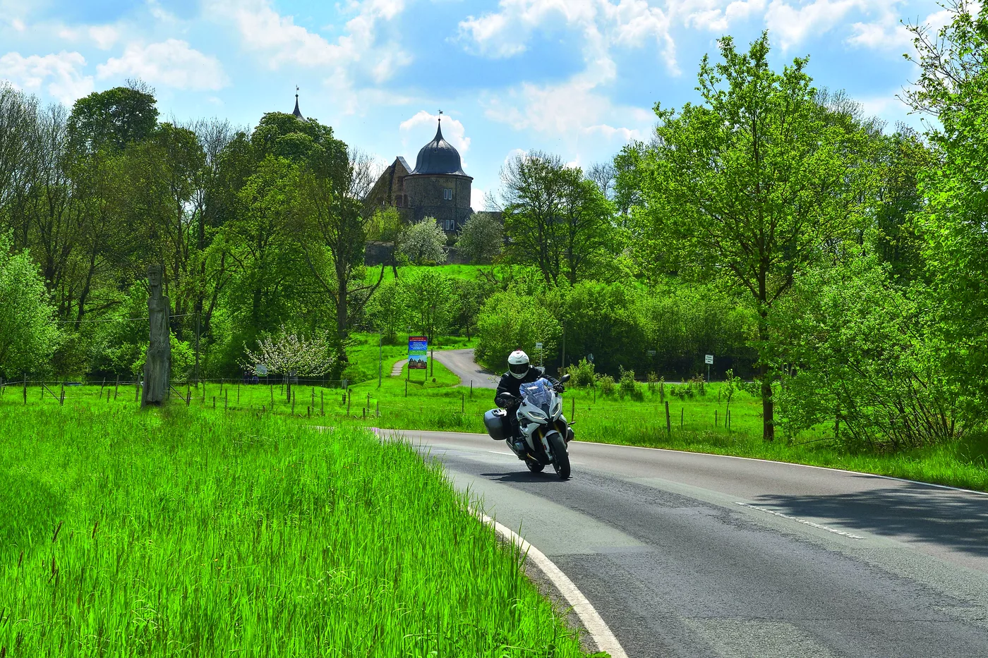 Motorrad auf der Landstraße, dahinter die Türme der Sababurg über den Wiesen