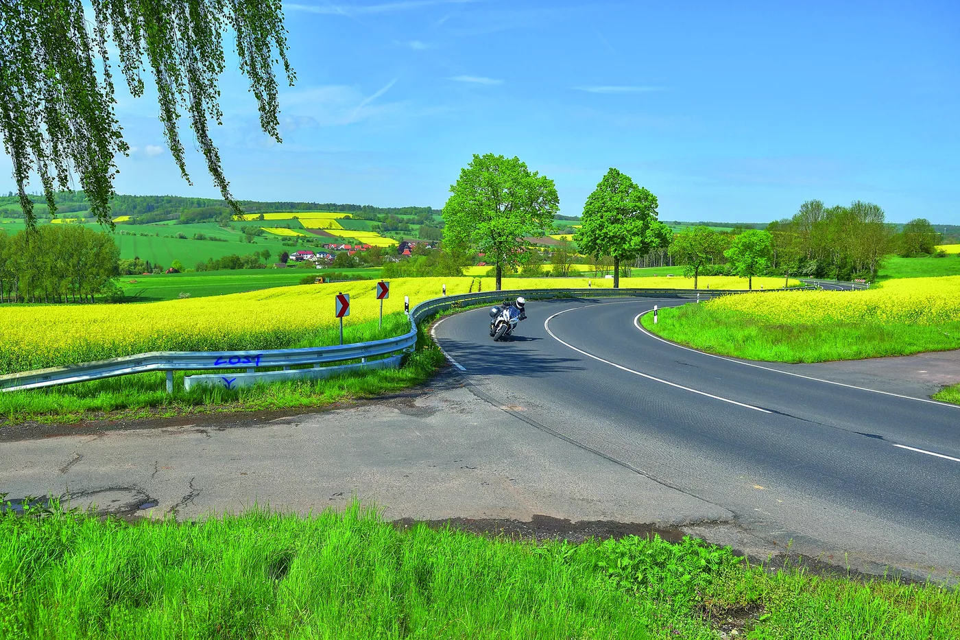 Motorrad auf einer Landstraße zwischen leuchtend gelben Rapsfeldern Motorrad auf einer Landstraße zwischen leuchtend gelben Rapsfeldern